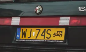 Numer rejestracyjny WJ-74S na zielonym Alfa Romeo 164. Widoczny znaczek Alfa Romeo i rysunek zabytkowego auta.