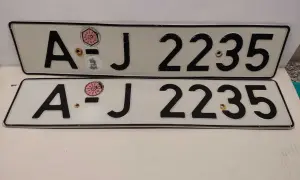 Dwie białe tablice rejestracyjne z czarnymi znakami "AJ 2235". Na górnej tablicy widoczna naklejka z numerem "11" w okręgu. To typowe niemieckie tablice rejestracyjne.