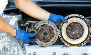 Mechanik w niebieskich rękawiczkach prezentuje części do wymiany sprzęgła: docisk i tarczę.