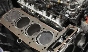 Nowa uszczelka pod głowicą czeka na montaż. Widać cylindry silnika i fragmenty osprzętu.