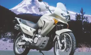 Jasnosrebrny motocykl Honda Transalp 650 gotowy na przygodę na tle ośnieżonej góry.