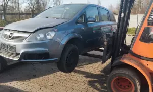 Szary Opel Zafira na złomowisku, podnoszony przez wózek widłowy. Dowiedz się, ile kosztuje złomowanie auta.