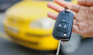 Kluczyk samochodowy z immobilizerem w dłoni, na tle żółtego auta.
