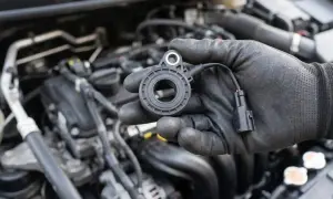 Mechanik w czarnej rękawiczce trzyma nowy czujnik spalania stukowego, gotowy do montażu w silniku samochodu.