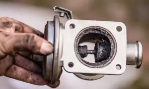Zatkany nagarem zawór EGR, który może powodować problemy z silnikiem. Brudne ręce mechanika sugerują trudną naprawę.
