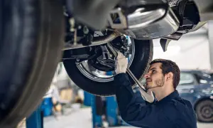 Mechanik w rękawiczkach naprawia podniesiony samochód. Zastanawiasz się, ile zarabia mechanik?