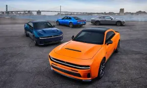 Pomarańczowy i niebieski Dodge Charger Hellcat z 2024 roku, obok szarego coupe, na tle mostu i miasta.