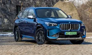 Błękitny BMW X1 elektryk z niebieskimi akcentami na progu, zaparkowany na kamienistej nawierzchni.