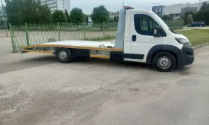 Biała laweta z platformą stoi na placu. Zastanawiasz się, ile kosztuje laweta?