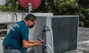 Technik sprawdza czujnik ciśnienia klimatyzacji, podłączając manometr do jednostki zewnętrznej.