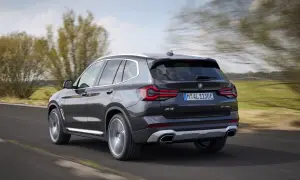 Ciemnoszary BMW X3 xDrive pędzi po drodze, otoczony zielenią i rozmazanymi drzewami.