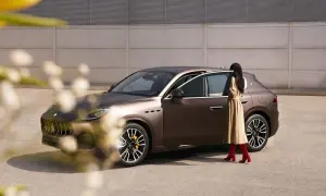 Elegancka kobieta w beżowej sukience i czerwonych kozakach wsiada do brązowego Maserati SUV.