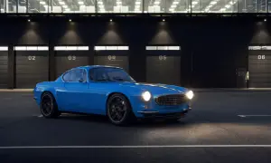 Niebieskie Volvo P1800 z nowoczesnymi felgami stoi przed budynkiem z numerowanymi bramami.
