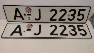 Dwie białe tablice rejestracyjne z czarnymi znakami "AJ 2235". Na górnej tablicy widoczna naklejka z numerem "11" w okręgu. To typowe niemieckie tablice rejestracyjne.