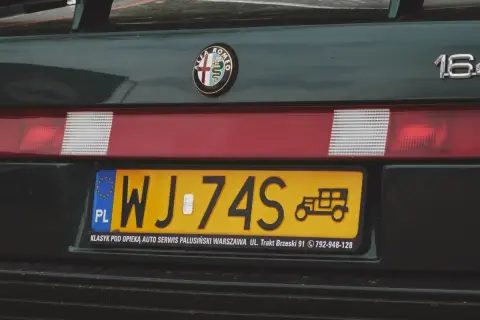 Numer rejestracyjny WJ-74S na zielonym Alfa Romeo 164. Widoczny znaczek Alfa Romeo i rysunek zabytkowego auta.