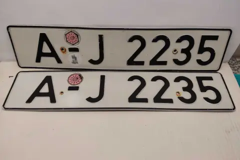 Dwie białe tablice rejestracyjne z czarnymi znakami "AJ 2235". Na górnej tablicy widoczna naklejka z numerem "11" w okręgu. To typowe niemieckie tablice rejestracyjne.