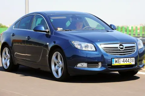Niebieski Opel Insignia 2.0 CDTI pędzi po drodze. Kierowca skupiony na trasie.
