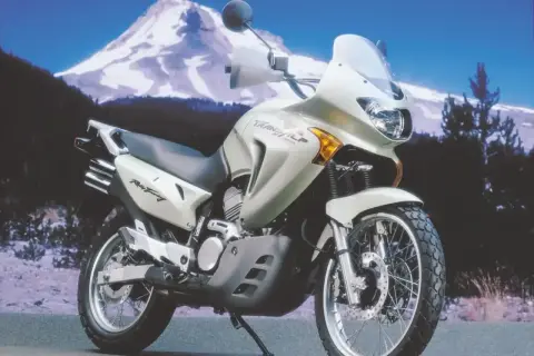Jasnosrebrny motocykl Honda Transalp 650 gotowy na przygodę na tle ośnieżonej góry.