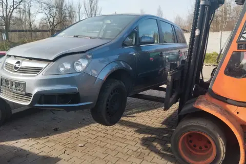 Szary Opel Zafira na złomowisku, podnoszony przez wózek widłowy. Dowiedz się, ile kosztuje złomowanie auta.