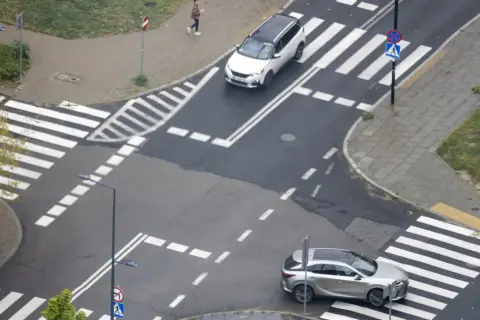 Skrzyżowanie z pasami i znakami drogowymi. Samochody zbliżają się do przejść, stosując zasadę prawej ręki.