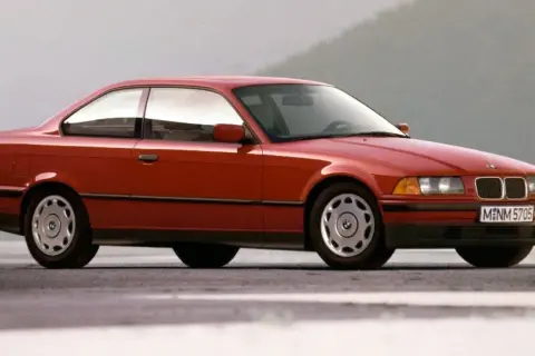 Czerwone BMW E36 coupe z lat 90. na tle szarego nieba. Klasyka motoryzacji.