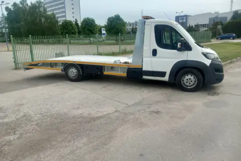 Biała laweta z platformą stoi na placu. Zastanawiasz się, ile kosztuje laweta?