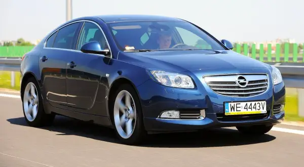 Niebieski Opel Insignia 2.0 CDTI pędzi po drodze. Kierowca skupiony na trasie.