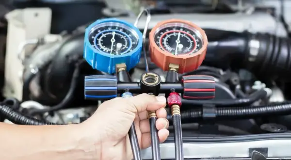 Mechanik sprawdza ciśnienie w układzie klimatyzacji. Dowiedz się, ile kosztuje nabicie klimatyzacji w Twoim samochodzie.