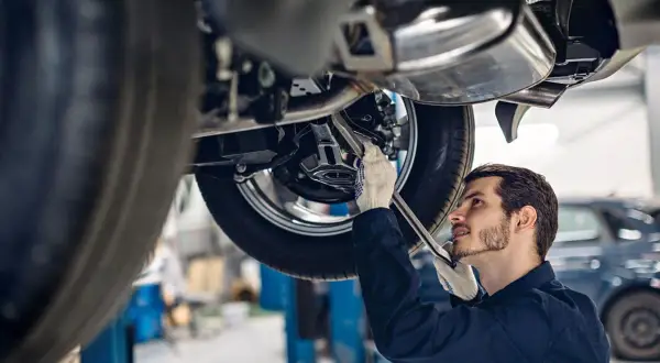 Mechanik w rękawiczkach naprawia podniesiony samochód. Zastanawiasz się, ile zarabia mechanik?