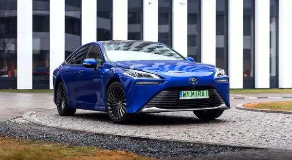 Niebieska Toyota Mirai, samochód przyszłości, zaparkowana przed nowoczesnym budynkiem.