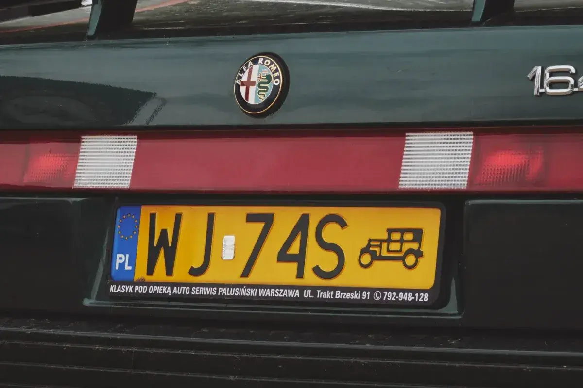 Numer rejestracyjny WJ-74S na zielonym Alfa Romeo 164. Widoczny znaczek Alfa Romeo i rysunek zabytkowego auta.