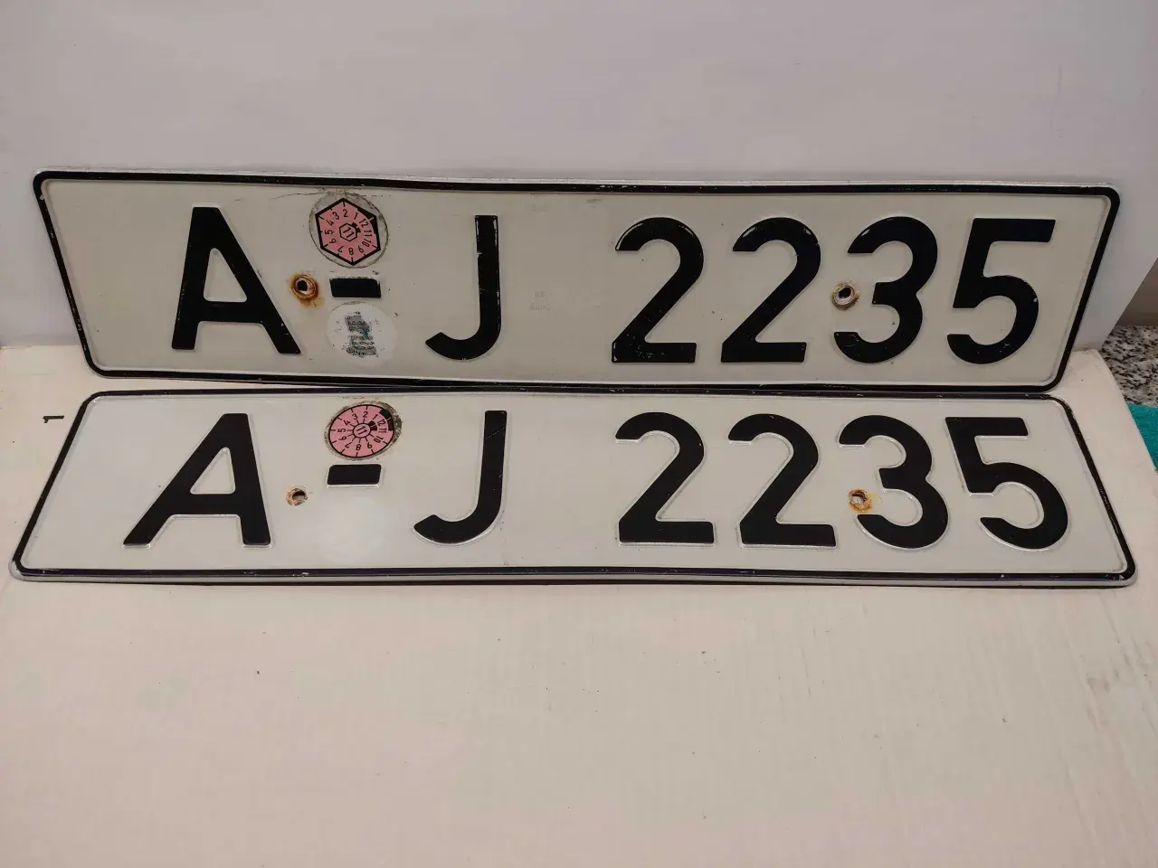 Dwie białe tablice rejestracyjne z czarnymi znakami "AJ 2235". Na górnej tablicy widoczna naklejka z numerem "11" w okręgu. To typowe niemieckie tablice rejestracyjne.