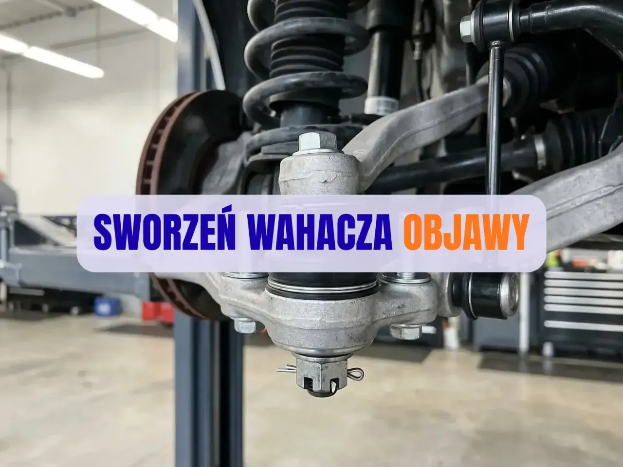 Widok na zawieszenie samochodu z widocznym sworzniem wahacza. Napis na obrazku: "SWORZEŃ WAHACZA OBJAWY".