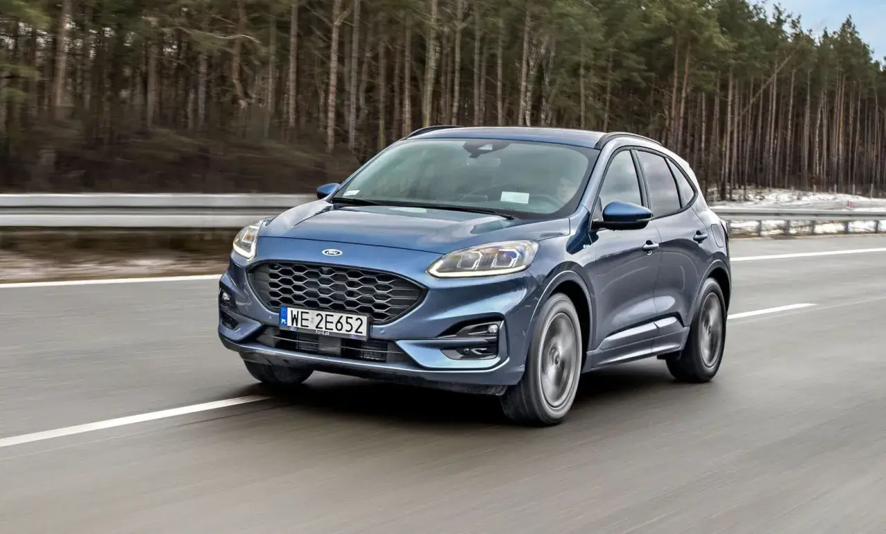 Niebieski Ford Kuga z silnikiem 1.5 Ecoboost pędzi po autostradzie wśród drzew.
