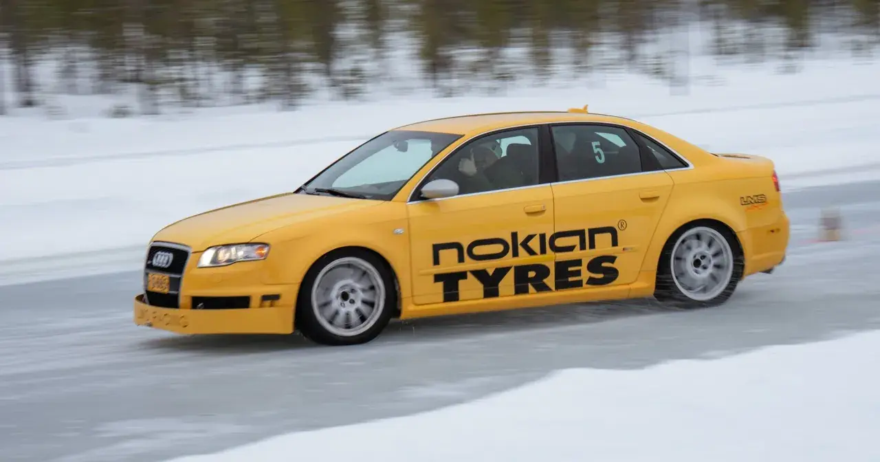Żółty Audi S1 Quattro z napisem "Nokian Tyres" śmiga po lodowym torze. Kierowca pokazuje kciuk w górę.
