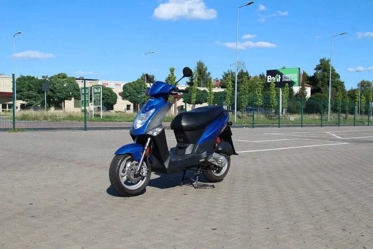 Niebieski skuter stoi na parkingu. Zastanawiasz się, czy na skuter trzeba mieć prawo jazdy?