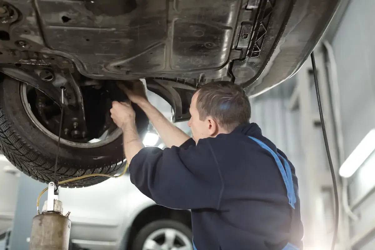 Mechanik wykonuje wymianę płynu hamulcowego, pracując pod podniesionym samochodem.