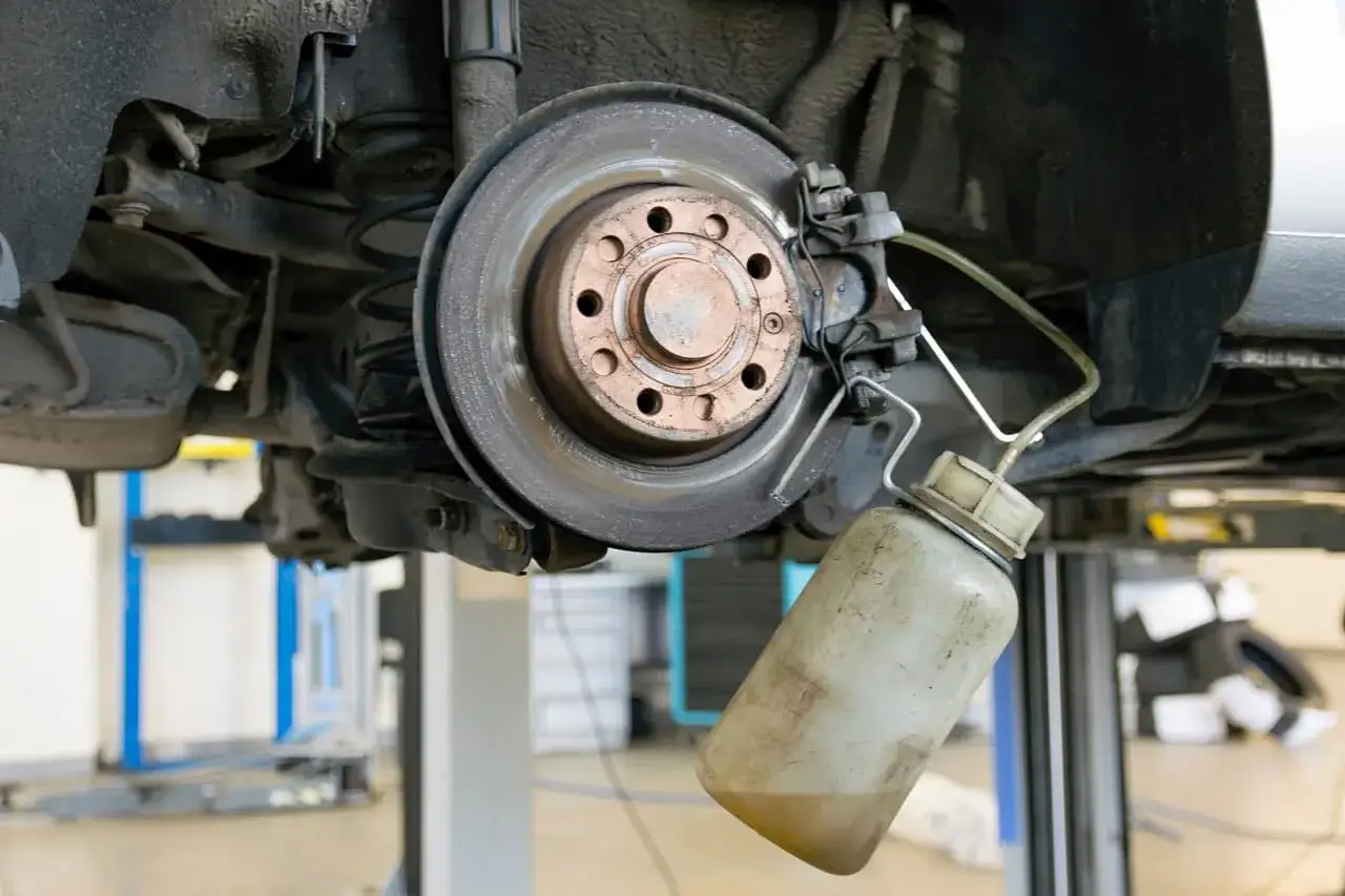 Mechanik przeprowadza odpowietrzanie hamulców, podłączając butelkę z płynem do zacisku hamulcowego przy tarczy.