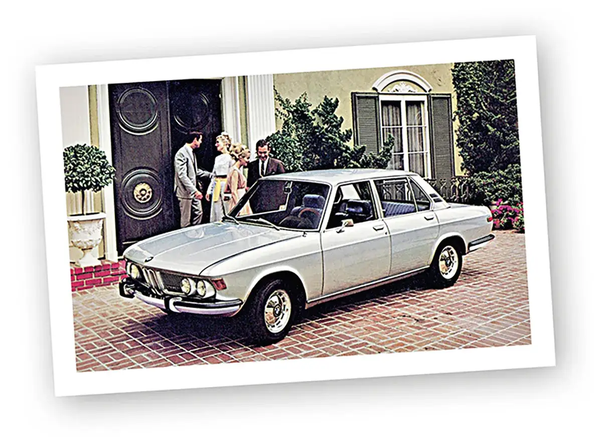 Elegancki, srebrny sedan BMW E9 z lat 70. stoi przed domem, gdzie czeka rodzina.