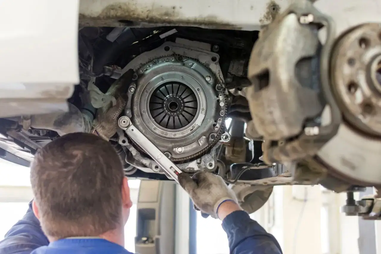 Mechanik dokonuje wymiany sprzęgła w samochodzie, używając klucza dynamometrycznego.