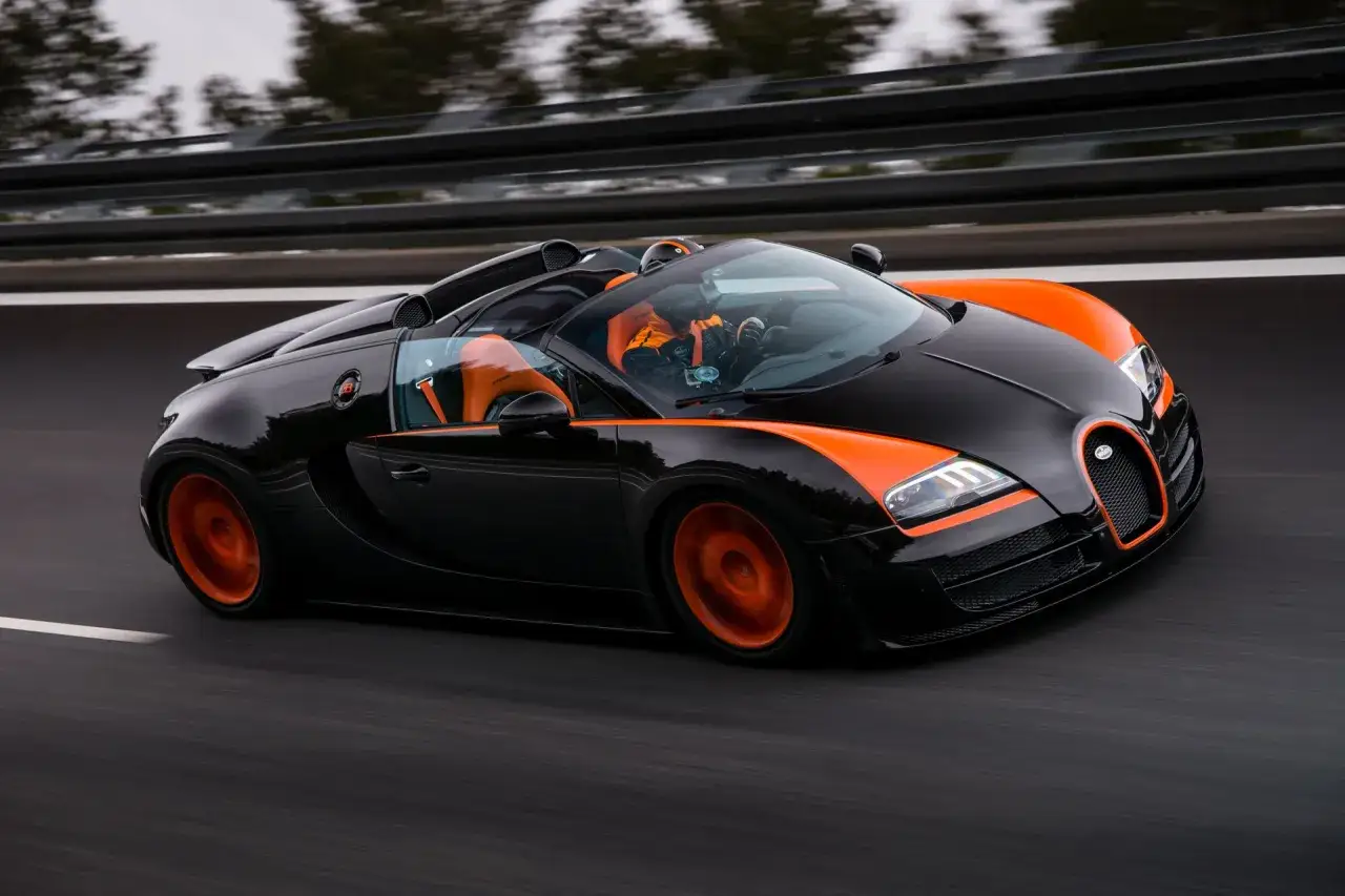 Czarny Bugatti Veyron z pomarańczowymi akcentami pędzi po drodze.
