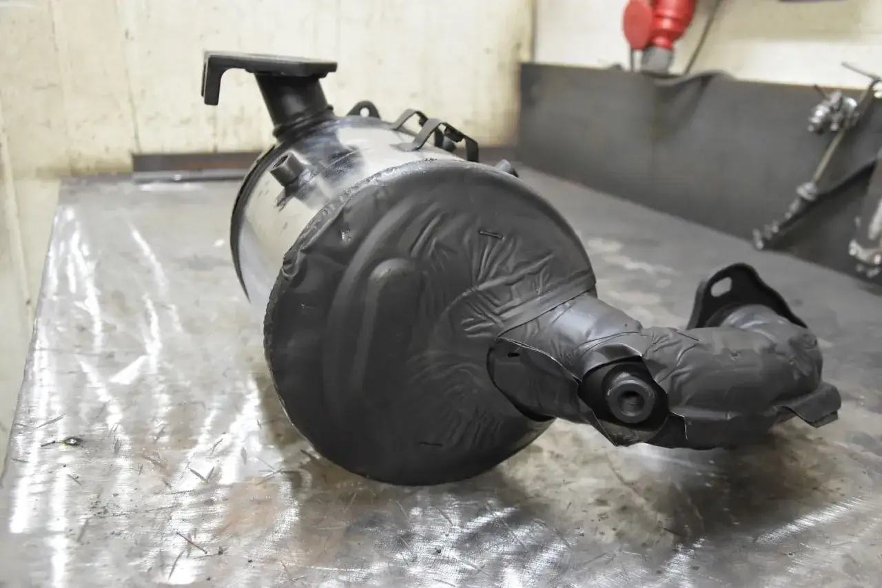 Element układu wydechowego, prawdopodobnie filtr DPF, owinięty czarną taśmą. Przygotowanie do wypalania DPF.