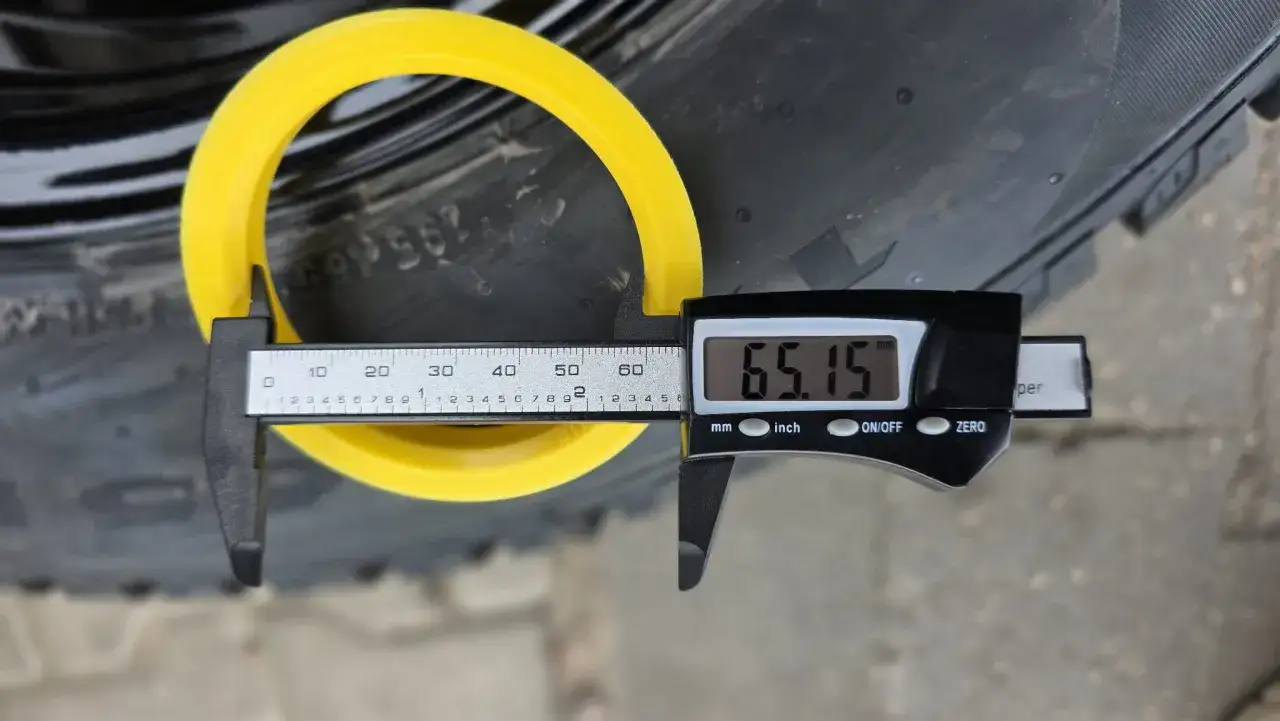 Żółty pierścień, prawdopodobnie otwór centrujący, mierzony suwmiarką cyfrową. Wynik pomiaru to 65.15 mm.
