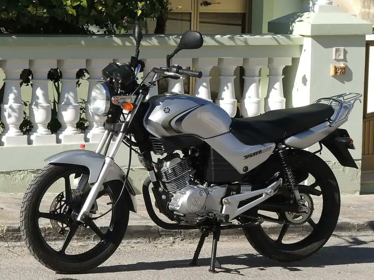 Srebrny motocykl Yamaha YBR 250 zaparkowany przed domem z białą balustradą.