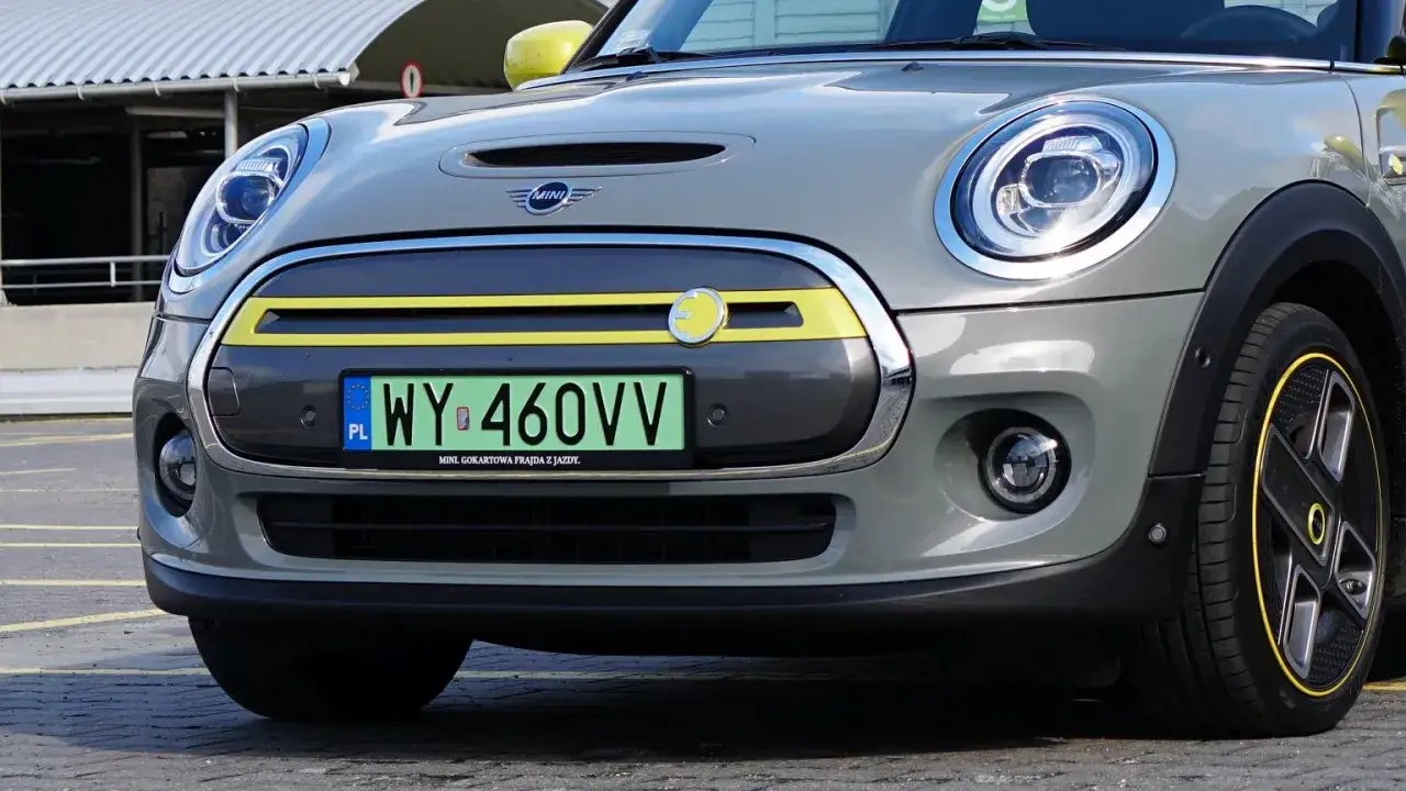 Szary Mini Cooper z żółtymi akcentami i zielonymi tablicami rejestracyjnymi.
