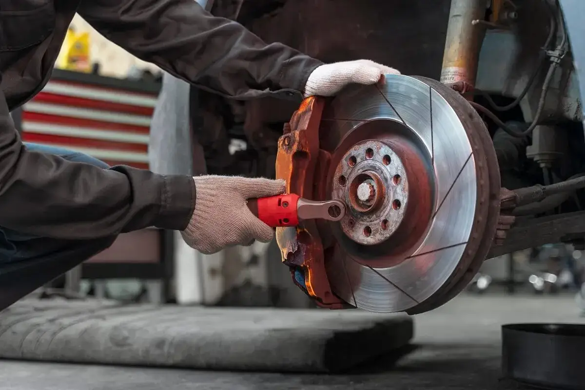Mechanik w rękawiczkach dokonuje wymiany klocków hamulcowych, używając klucza do odkręcenia śruby.