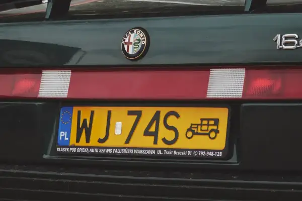 Numer rejestracyjny WJ-74S na zielonym Alfa Romeo 164. Widoczny znaczek Alfa Romeo i rysunek zabytkowego auta.