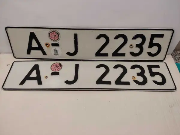 Dwie białe tablice rejestracyjne z czarnymi znakami "AJ 2235". Na górnej tablicy widoczna naklejka z numerem "11" w okręgu. To typowe niemieckie tablice rejestracyjne.