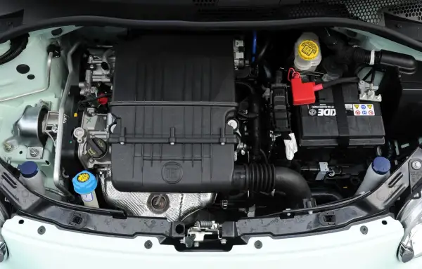Silnik w fiat 500 l. Widoczny akumulator, osłona silnika z logo FIAT, zbiorniczki płynów i elementy układu dolotowego.