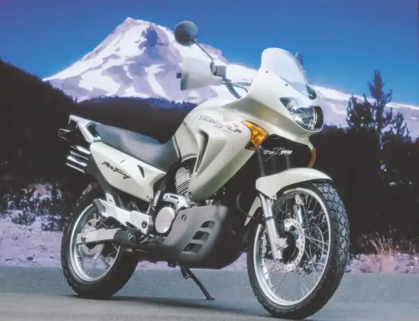 Jasnosrebrny motocykl Honda Transalp 650 gotowy na przygodę na tle ośnieżonej góry.